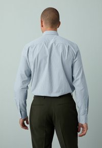 Hellblau gestreiftes Hemd mit langen Ärmeln und Manschetten, kombiniert mit dunkelgrünen Hosen. Hat einen klassischen Kragen und Knopfdetails.