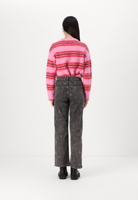 Vaaleanpunainen ja punainen raidallinen pörröinen neule yhdistetty korkeavyötäröisiin haalistuneisiin mustiin farkkuihin, joissa on tähtikuvioita, ja mustiin paksupohjaisiin kenkiin.