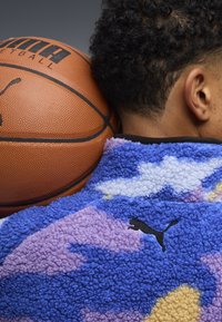 Maglione in pile blu, viola e crema, con motivo a nuvole e logo Puma nero, posizionato accanto a un pallone da basket.