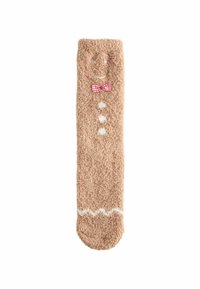 Weiche, beige Socke mit flauschiger Textur. Sie hat ein lächelndes Gesicht, eine rot karierte Fliege, weiße Knöpfe und ein Zickzackmuster am Boden.