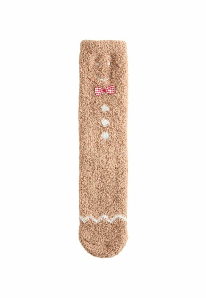 Weiche, beige Socke mit flauschiger Textur. Sie hat ein lächelndes Gesicht, eine rot karierte Fliege, weiße Knöpfe und ein Zickzackmuster am Boden.