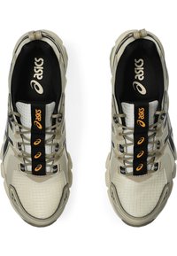 Baskets de sport beiges avec une tige en maille texturée, présentant des accents noirs et oranges, et un design de semelle épaisse.