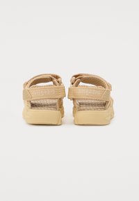 Beige gewebte Sandalen mit zwei verstellbaren Riemen, strukturiertem Fußbett und Gummisohle. Mit Markenlogo auf dem hinteren Riemen.