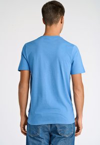 Himmelsblå bomullströja med korta ärmar, rundad halsringning och en mjuk textur. Bakifrån syns en rak skärning i fållen och inga synliga logotyper.