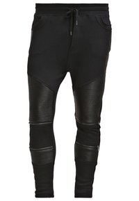 Svarta joggebukser i ett slätt tyg med ribbade detaljer vid knäna, exponerade dragkedjor och elasticitet med snörning i midjan.