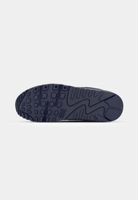 Marinblå sneaker sula med texturerad gummi, som har ett mönster, varumärkning och uttalade spår för grepp.