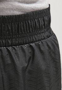 Czarne, sportowe spodenki z teksturowanym wzorem, elastycznym pasem i lekkim materiałem zaprojektowane dla wygody i elastyczności.