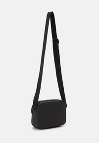 Črn crossbody nahrbtnik s gladko teksturo, pravokotno obliko, nastavljivim trakom in zadrgo na vrhu. Minimalistična zasnova brez vidne strojne opreme.