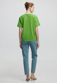 Maglietta in cotone verde con maniche corte, vestibilità rilassata e scollatura rotonda, abbinata a jeans a gamba dritta blu chiaro e tacchi beige.