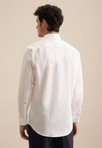 Witte langemouwen shirt van gladde stof, met een standaardkraag, afgeronde zoom en knoopsluiting met subtiele zwarte details.
