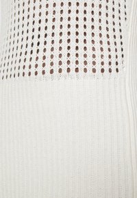 Witte gebreide stof met een textuurontwerp met open, ronde patronen en verticale ribbels aan de onderkant, wat een lichte, luchtige uitstraling geeft.