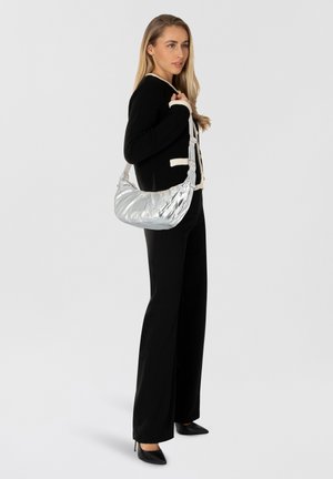 Silberne Schultertasche mit einer gesteppten Textur, kombiniert mit einem schwarzen Strickcardigan und schwarzen Hosen. Die Tasche verfügt über einen einzigen Riemen.