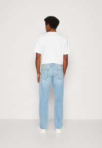 Camiseta blanca de manga corta con cuello redondo, combinada con jeans rectos de color azul claro. Ambas prendas tienen un corte relajado.