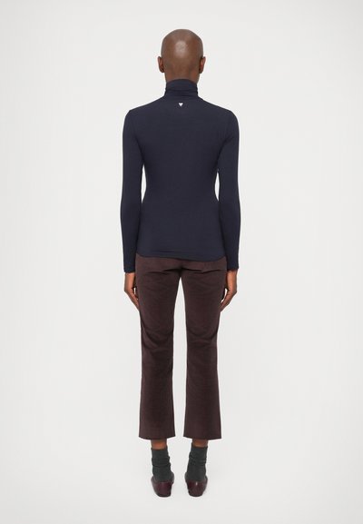Navy niebieski sweter typu golf z długim rękawem, połączony z burgundowymi spodniami o szerokich nogawkach i szarymi skarpetkami do kostek. Prosty design, gładka faktura.