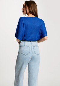 Blau glitzerndes kurzärmeliges Strickoberteil, kombiniert mit hochtaillierten hellblauen Jeans im gerade geschnittenen Schnitt und mit Fünf-Taschen-Design.