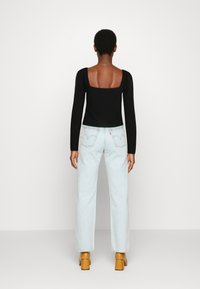 Camisola preta de mangas longas com costas quadradas, combinada com jeans de cintura alta azul claro e saltos robustos castanhos. Design simples, sem padrão.