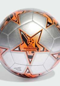 Palla da calcio argento con motivi a stella arancioni e neri, logo della UEFA Champions League e testo "Replica Match Ball Club".