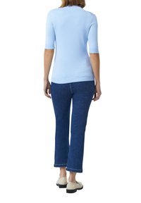 Hellblaues, kurzärmliges Sweater, taillierte Passform, kombiniert mit dunkelblauen Jeans, mit geradem Beinschnitt und leicht verkürzter Länge. Flache, cremefarbene Schuhe.