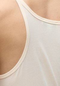 Κοντινό πλάνο ενός ατόμου που φοράει λευκό αμάνικο τοπ, δείχνοντας τον ώμο και την άνω πλάτη.