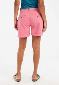 Roze katoenen shorts met opgerolde zoom, voorzien van achterzakken en een gestreepte tailleband. Draagt met tan sandalen.