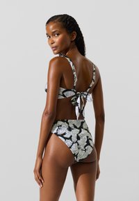 To-delt badedragt med et sort og hvidt bladmønster, justerbare stropper og en knyttet lukning bagpå. Højtaljet design på underdelen.