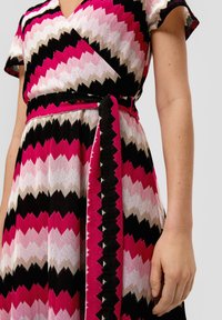 Kleid in knielanger Form mit einem Zickzackmuster in Rosa, Schwarz und Creme. Hergestellt aus strukturiertem Stoff mit Wickeldesign und passendem Gürtel.