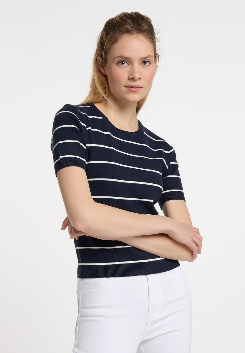 Marineblauer Strickpullover mit weißen horizontalen Streifen, kurzen Ärmeln und Rundhalsausschnitt. Getragen mit weißen Hosen, glatte Textur.