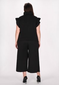 Sort outfit bestående af en struktureret top med flæser på ærmerne og brede bukser. Fremstillet af tekstureret stof, parret med sorte højhælede sko.