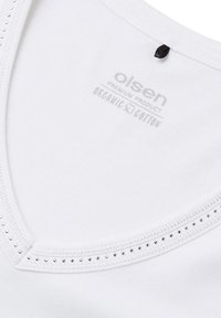 Witte biologische katoenen t-shirt met V-hals, voorzien van een rij kleine zilveren studs langs de halslijn en een label aan de binnenkant.