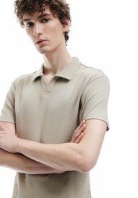 Beige ribbet polo skjorte med korte ærmer, der har en klassisk krave og en tekstureret overflade, der elegant sidder tæt til kroppen.