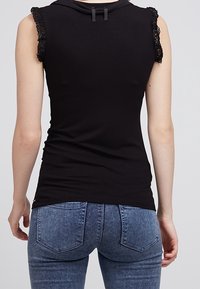 Svart ärmlös topp med spetsdetaljer vid axlarna, med en åtsittande design. Bärs med blå denimjeans som visar detaljerna i ryggen och fickorna.