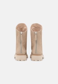 Beige semišové kotníkové boty s hladkou texturou, předními zipy a robustními gumovými podrážkami. Design má zaoblený vršek a minimální detaily.