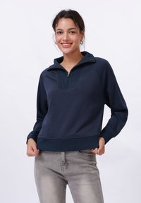 Mørkeblå kvart-zip sweatshirt med ribbestrikket krage, myk tekstur og tettsittende mansjetter. Har et panelert design med en avslappet passform.