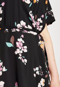 Blumenkleid aus leichtem schwarzem Stoff mit rosa, weißen, orangefarbenen und türkisfarbenen Blumen; Taillengürtel mit entspannter Passform und kurzen Ärmeln.