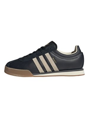 Czarny sneaker Adidas z beżowymi paskami, gumową podeszwą i sznurowanym fasonem, pokazany w profilu na białym tle.