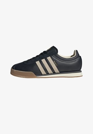 Baskets Adidas noires avec des bandes beiges, semelle en gomme et design à lacets, vues de profil sur fond blanc.