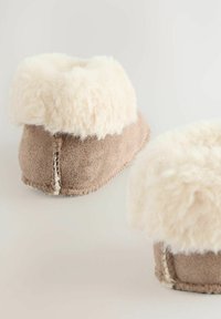 Chaussons en suede tan avec une large bordure en fourrure crème duveteuse, présentant un détail de couture le long de la semelle. Texture douce et forme arrondie.