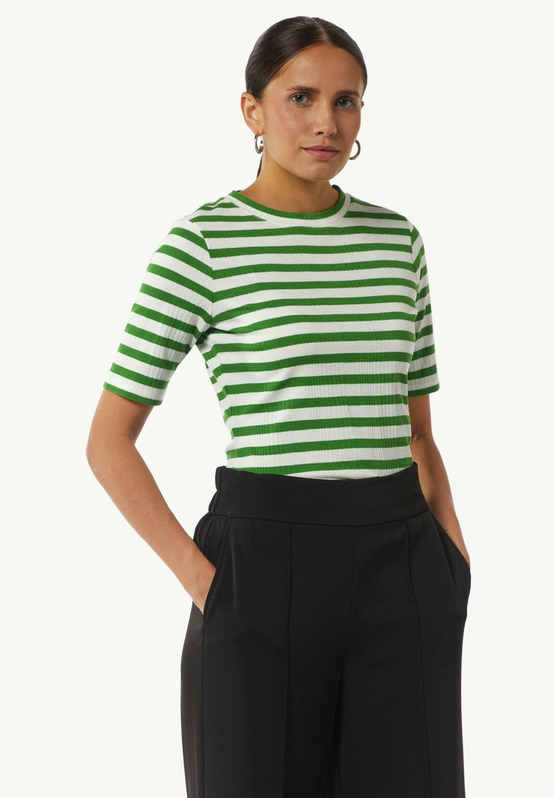 Grünes und weiß gestreiftes Rippenstrickshirt mit Rundhalsausschnitt und kurzen Ärmeln, kombiniert mit hochtaillierten schwarzen Hosen mit Seitentaschen.