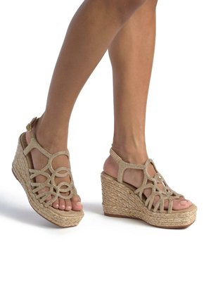 Sandali con zeppa beige con base in paglia intrecciata e design decorativo a intaglio. Cinturino alla caviglia regolabile con accenti metallici. Stile open-toe.