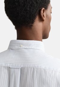 Hellblau gestreiftes Hemd mit spitzem Kragen, das einen Knopf am Nacken und eine Falte in der Mitte des Rückens aufweist.