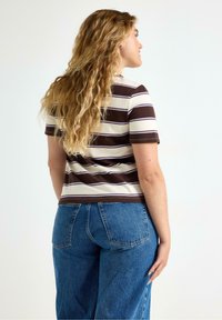 Maglietta a righe nei colori marrone e crema, maniche corte e design aderente, abbinata a jeans blu a vita alta.