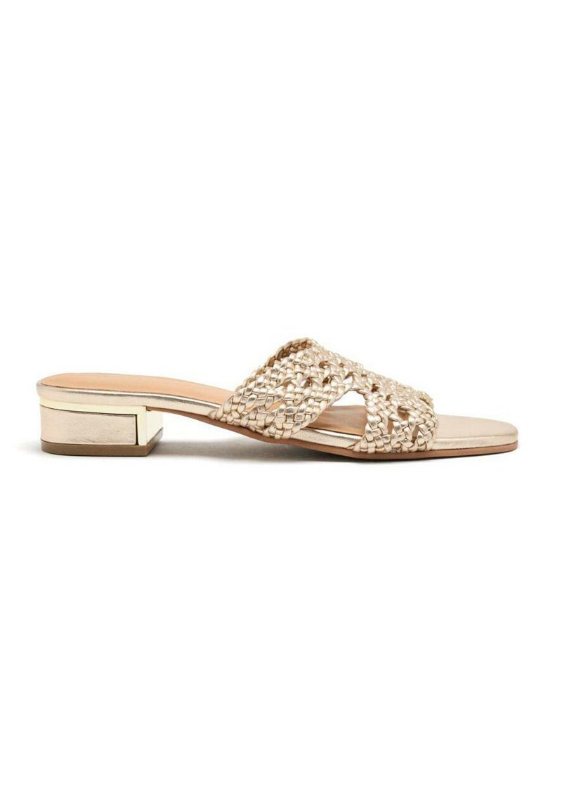 Sandalias deslizantes en beige tejido con un tacón bajo. Presenta un diseño de correas cruzadas y una plantilla de cuero suave con un acento metálico en el tacón.