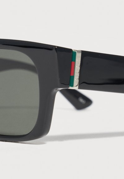 Μαύρα ορθογώνια γυαλιά ηλίου με ασημένια λεπτομέρεια μεντεσέ που διαθέτει πράσινες και κόκκινες ρίγες στο κλαδάκι.