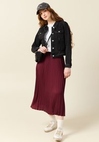 Jeansjacka, vit t-shirt, bordeauxfärgad plisserad midi-kjol, vita sneakers med beige detaljer och en grå keps. Enkel, avslappnad outfit.