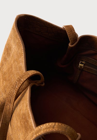 Καφέ υφασμάτινη τσάντα από δέρμα με δύο χερούλια, ανοιχτή κορυφή και μια μικρή εσωτερική τσέπη με φερμουάρ ορατή στο εσωτερικό.