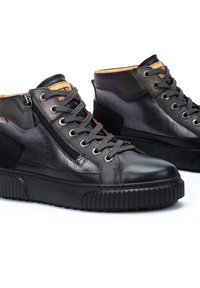 Zapatillas altas de cuero negro con cierre de cremallera, parte delantera con cordones, suela de goma texturizada y forro interior en contraste de color marrón.