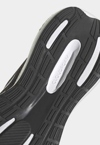 La suela de la zapatilla presenta un diseño de goma negra texturizada con acentos blancos, un logo en relieve de "CLOUDfoam" y varios patrones de agarre para mayor tracción.