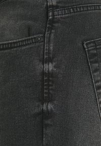 Schwarze Denim-Jeans mit glatter Textur, sichtbaren Nähten, einer kleinen Fronttasche und einem standardmäßigen Design der Gesäßtasche.