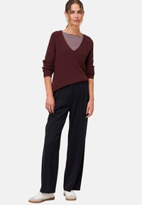 Maroon knitted sweater with a deep V-neck over a striped top, paired with high-waisted black trousers and white sneakers.