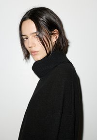 Schwarzer Rollkragenpullover aus weichem Strickstoff mit geripptem Kragen und lockerer Passform, minimalistische Details und glatte Textur.